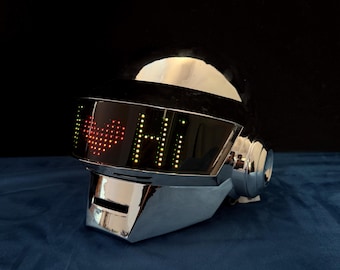 Op de afbeelding: Een glanzende helm met chroomafwerking en een donker vizier met een digitaal led-display. Het display toont een rood gepixeld hartsymbool gevolgd door de tekst "HI" in het geel, verlicht tegen het donkere vizieroppervlak.