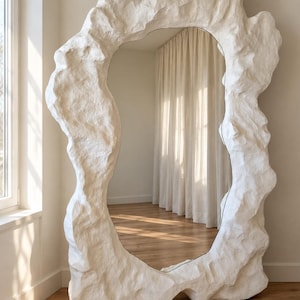 May include: A large floor mirror featuring an irregular, organic frame with a textured, matte white finish that resembles natural rock or stone formations. The central reflective glass surface is shaped to follow the uneven contours of the frame.