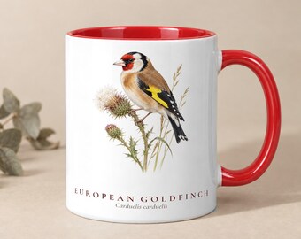 Könnte beinhalten: Ein weißer Keramikbecher mit leuchtend rotem Innenraum und Henkel. Die Außenseite zeigt eine detaillierte Illustration eines Stieglitz auf einer Distelpflanze, mit dem Text "EUROPEAN GOLDFINCH Carduelis carduelis" darunter.