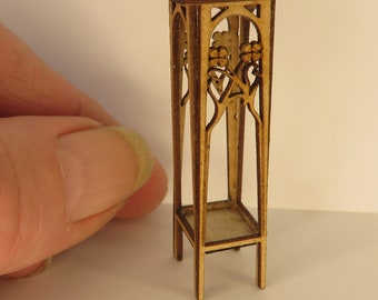 Puede incluir: Un soporte de madera en miniatura con una parte superior de color marrón oscuro y tallas intrincadas. El soporte tiene un estante y está hecho de madera marrón claro.