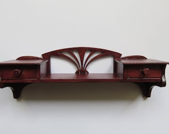 May include: A dark cherry-stained wooden wall shelf with two small drawers and a decorative fan-shaped back. The shelf has a simple, elegant design, perfect for displaying small items. The drawers have round knobs.