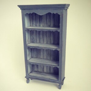 May include: A dark blue wooden bookcase with four shelves. The shelves have a decorative scalloped edge and the bookcase has turned legs.
