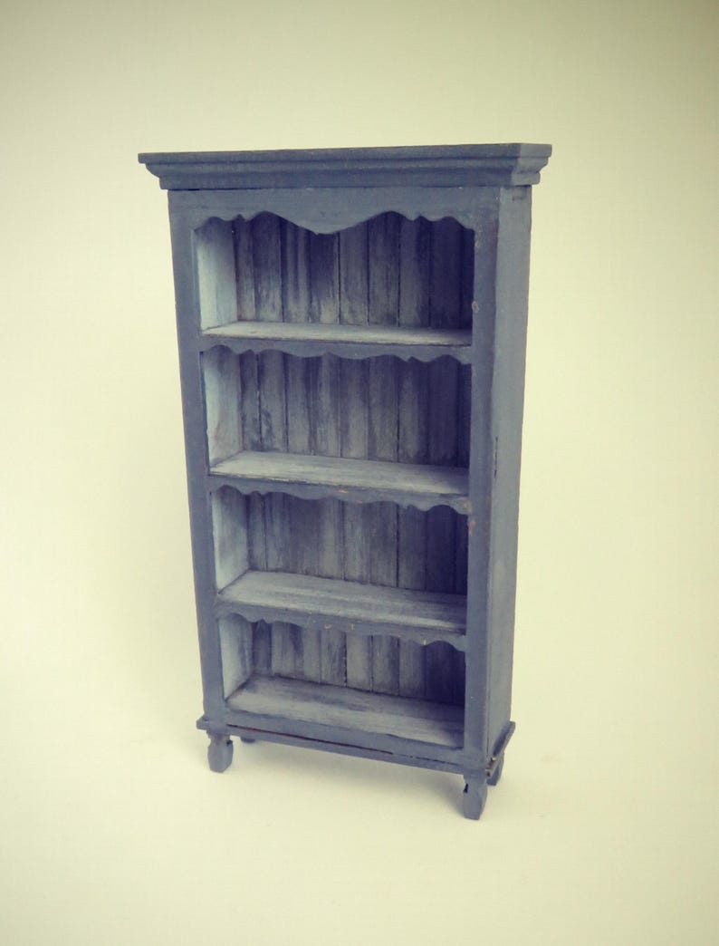 May include: A dark blue wooden bookcase with four shelves. The shelves have a decorative scalloped edge and the bookcase has turned legs.