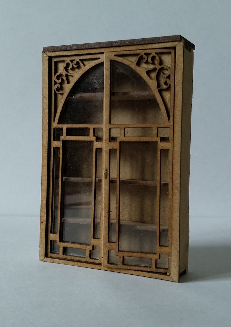 May include: A wooden cabinet with glass doors and shelves. The cabinet has a decorative design on the top and sides. The cabinet is made of light brown wood.