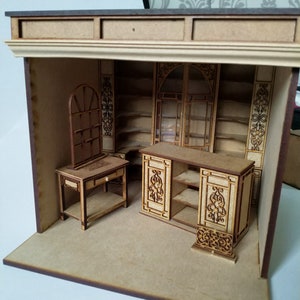 May include: A miniature wooden model of a shop interior with shelves, a counter, and a small table with a mirror. The model is made of light brown wood and has intricate details.