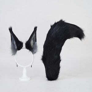 May include: A set of faux fur animal ears attached to a thin headband and a matching long faux fur tail. The ears are black with grey inner accents, and the tail is solid black. Both pieces feature long, soft, synthetic fibers.