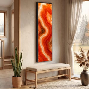 Puede incluir: Una pieza de arte mural rectangular y vertical que presenta un patrón abstracto de piedra ágata con bandas onduladas en tonos naranja brillante, rojo intenso y blanco crema, encerrada en un marco negro fino y sencillo.