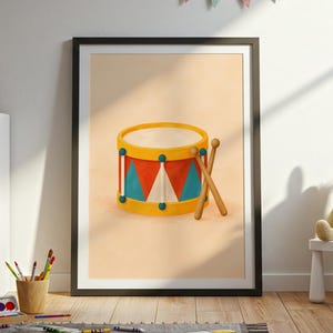 May include: A framed wall art print featuring a centered illustration of a yellow, red, and teal drum with two wooden drumsticks resting against it. The drum has a geometric pattern of triangles and blue circular accents on a light peach background.