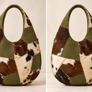 May include: A hobo-style handbag featuring a patchwork design of olive green fabric panels and brown, black, and white cowhide sections. The bag has a rounded silhouette with an integrated handle and small metallic rivets on the sides.
