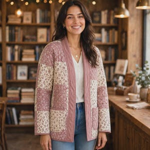 May include: A quilted jacket featuring a patchwork design of dusty rose and cream floral fabric. The jacket has an open front with a solid dusty rose trim, long sleeves, and two square patch pockets on the front, worn over a white top.