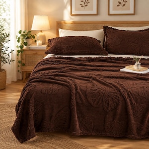 May include: A dark brown bedding set featuring a textured butterfly pattern. The set includes a large, plush throw blanket draped over the bed and two matching rectangular pillow shams, all displaying a raised, embossed butterfly motif.
