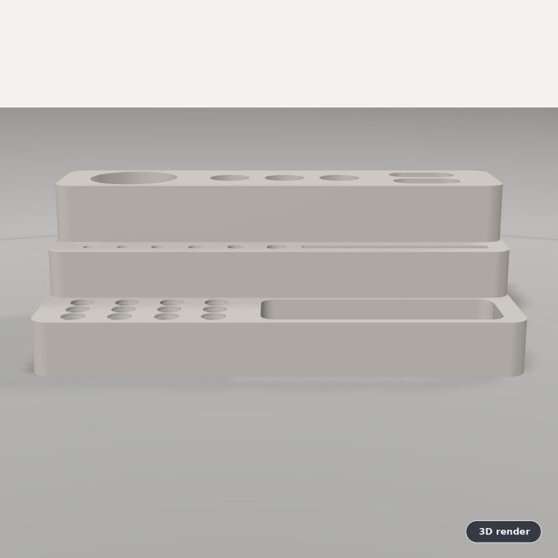 Puede incluir: Un organizador de escritorio escalonado de color gris claro con m&uacute;ltiples orificios circulares de varios tama&ntilde;os en los niveles superior y medio, adem&aacute;s de una ranura rectangular larga y un compartimento en el nivel inferior.