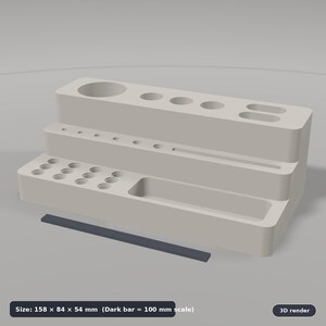 Puede incluir: Un organizador de escritorio escalonado de color gris claro con m&uacute;ltiples aberturas circulares y rectangulares para almacenamiento. La unidad mide 158 x 84 x 54 mm, con una barra oscura que indica una escala de 100 mm. Render 3D.