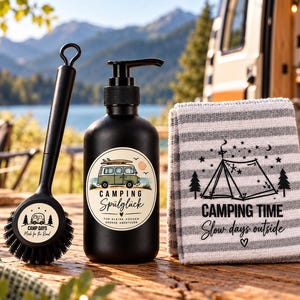 Könnte beinhalten: Eine schwarze Spülbürste, ein schwarzer Seifenspender mit einem Etikett, das einen grünen Campingbus und den Text "CAMPING Spülglück" zeigt, sowie ein grau-weiß gestreiftes Küchentuch mit einer schwarzen Zeltgrafik und dem Text "CAMPING TIME Slow days outside".
