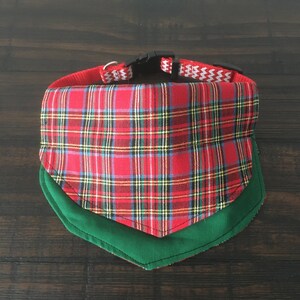May include: Red and green plaid dog bandana with a green trim. The bandana is attached to a black and white patterned collar.