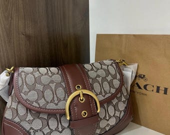 Könnte beinhalten: Eine braun-beige Umhängetasche mit wiederholtem Logomuster auf dem Stoffkörper, akzentuiert durch glatte braune Lederbesätze und einen markanten goldfarbenen Metallschnallenverschluss an der Frontklappe. Die Tasche hat goldene Beschläge.