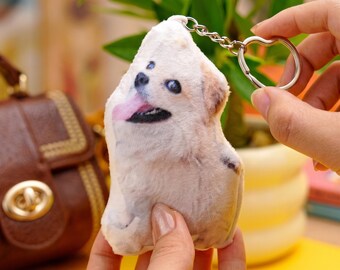 May include: A plush keychain featuring a printed image of a light-colored dog with its tongue sticking out. The soft, stuffed dog figure is attached to a silver-toned metal split ring and a short chain, designed for use as a decorative accessory.