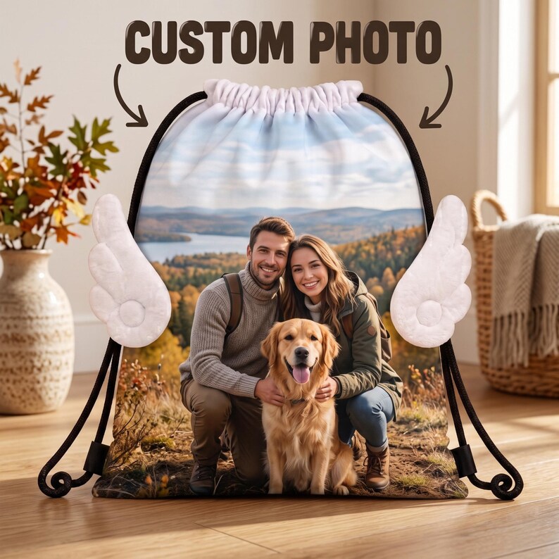 May include: A drawstring backpack featuring a custom photo of a couple and a golden retriever outdoors. The bag has white plush angel wings attached to the sides, black drawstrings, and the text CUSTOM PHOTO printed at the top.
