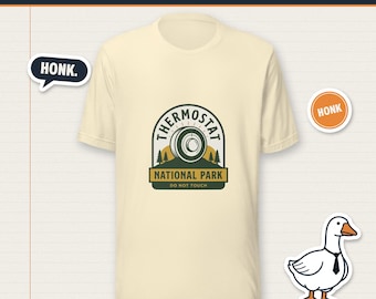 May include: A cream-colored short-sleeve t-shirt featuring a graphic of a thermostat dial above the text THERMOSTAT NATIONAL PARK DO NOT TOUCH. The design includes pine trees and a sun. A white goose wearing a black tie is also visible.