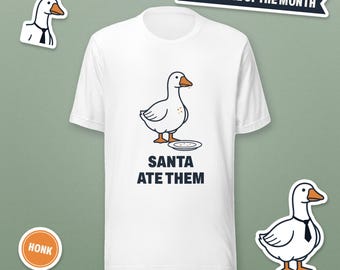 May include: A white short-sleeve t-shirt featuring a graphic of a goose standing by a plate with the text SANTA ATE THEM. Additional graphics include a goose wearing a tie, a HONK circle, an EMPLOYEE OF THE MONTH banner, and HONK INDUSTRIES text.
