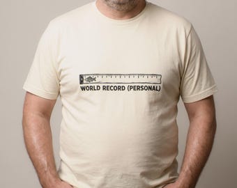 Op de afbeelding: Een crèmekleurig T-shirt met korte mouwen en een zwarte afbeelding van een liniaal met een klein visicoontje aan het begin. Onder de liniaal staat de tekst "WORLD RECORD (PERSONAL)" in een vetgedrukt, gecentreerd lettertype.