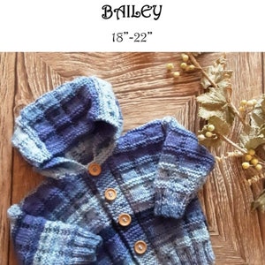 Puede incluir: Un cárdigan de punto azul y blanco a cuadros para bebé con capucha y cierre de botones. El cárdigan está colocado sobre una superficie de madera. El texto "Prickles & Whiskers Baby Designs Bailey 18"-22"" es visible en la parte superior de la imagen.
