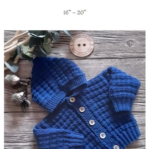 May include: A knitted blue baby cardigan and matching hat set. The set features a textured stitch pattern and is fastened with white buttons. The text "Prickles & Whiskers Baby Designs Quaid" is at the top. The size is 40.6cm-50.8cm.