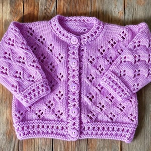 May include: A light purple knitted cardigan featuring a delicate openwork diamond pattern, long sleeves with ribbed cuffs, a round neckline, and a front button closure with five matching circular buttons.