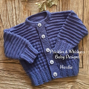 Könnte beinhalten: Ein lila gestrickter Baby-Cardigan mit weißen Knöpfen. Der Cardigan hat ein Zopfmuster und ist aus weichem Garn gefertigt. Der Text "Prickles & Whiskers Baby Designs" und "Hardie" ist auf dem Cardigan sichtbar.