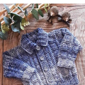 May include: A blue and white knitted cardigan with a collared neckline and button closure. The text "Yale" and "18"-22" is visible. The sweater is made of a textured yarn and is displayed on a wooden surface.
