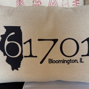 May include: A beige pillow with a black outline of the state of Illinois and the numbers "61701" with the text "Bloomington, IL" below.