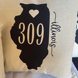 May include: Beige pillow with a black outline of the state of Illinois, a white heart, and the text "309 Illinois".