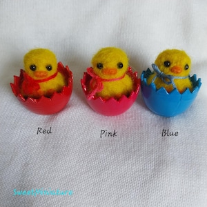 May include: Three felt chicks in eggshells, each with a different colored eggshell: red, pink, and blue. The chicks are yellow with black eyes and beaks.