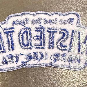 May include: A white embroidered patch with a scalloped edge featuring the blue text TWISTED TEA in a bold, stylised font. The design includes smaller blue text above and below the main brand name, all rendered in a clean, stitched thread finish.