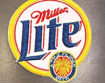 May include: A circular embroidered patch featuring the Miller Lite logo in red and blue on a white background with a yellow border. A smaller circular emblem at the bottom displays a golden wheat stalk graphic with the text A FINE PILSNER BEER.