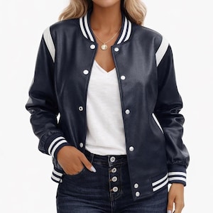Könnte beinhalten: Eine marineblaue Collegejacke mit weiß gestreiften Rippbündchen an Kragen, Ärmeln und Saum. Die Jacke verfügt über eine Druckknopfleiste und weiße Einsätze an den Schultern sowie Ärmeln, getragen über einem schlichten weißen V-Ausschnitt-Shirt.