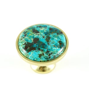 Może przedstawiać: Okrągły, turkusowy i brązowy, wzorzysty gałka z podstawą w kolorze złotym. Gałka wykonana jest z kamienia i metalu.