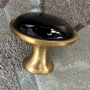 May include: A black ceramic knob with a brass base. The knob is round and has a smooth, glossy finish.
