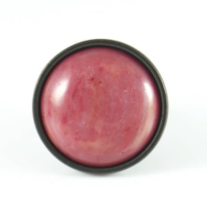 May include: A round, pink cabochon ring with a black metal setting.