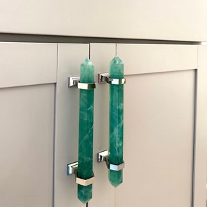 Op de afbeelding: Twee groene kristallen kastgrepen met een zilveren afwerking. De grepen zijn gevormd als een puntig kristal en hebben een zilveren band rond het midden.