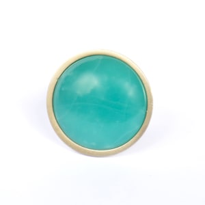 Może przedstawiać: Okrągły, turkusowy kaboszon osadzony w złotej obrączce.