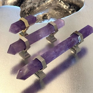 May include: Three amethyst crystal cabinet pulls with gold accents and silver bases. The pulls are arranged in a staggered pattern on a silver surface.