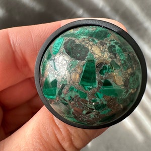 May include: A round, black, decorative knob with a green and gold malachite stone inlay.