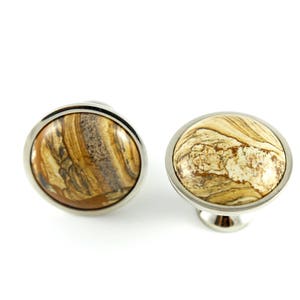May include: Two round cabinet knobs with a silver metal base and a brown and white marbled stone top.