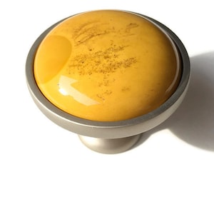 Può includere: Un pomello per armadio rotondo in vetro giallo con una base in metallo argentato.