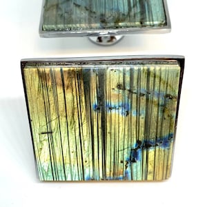 May include: Square cabinet knob with a green, blue and gold iridescent labradorite stone inlay. The knob has a silver metal frame.