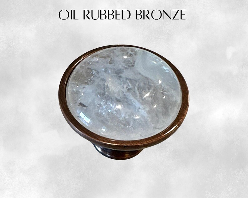 K&ouml;nnte beinhalten: Ein runder, klarer Kristall-Schrankknopf mit einer &ouml;lge&ouml;lten Bronzebasis. Der Knopf hat eine strukturierte Oberfl&auml;che und eine glatte, polierte Oberfl&auml;che.