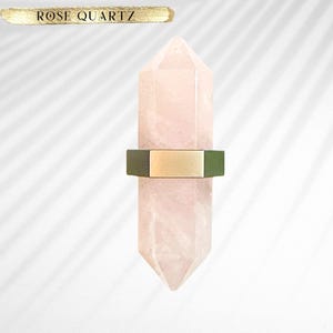 May include: A rose quartz crystal with a gold and green metal accent. The crystal is shaped like a point and is a light pink color.
