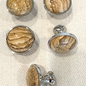 May include: Five cabinet knobs with a chrome finish and a brown and beige stone inlay. Two knobs are round and three knobs have a post for mounting.