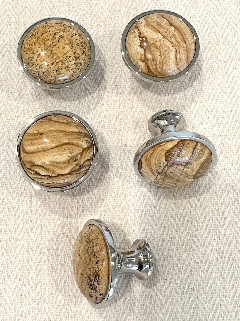 May include: Five cabinet knobs with a chrome finish and a brown and beige stone inlay. Two knobs are round and three knobs have a post for mounting.
